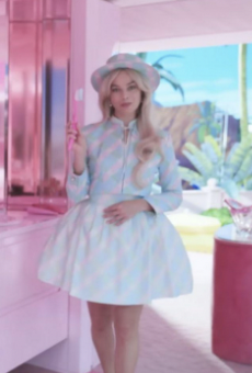 Still from Barbie (2023): Barbie stands inside the pink Dreamhouse wearing a striped blue-and-white outfit and matching hat, holding a pink brush